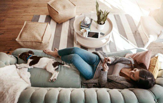 Mulher relaxando no sofá de casa com cachorro - Cidades do Quinto Andar