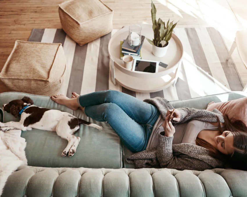 Mulher relaxando no sofá de casa com cachorro - Cidades do Quinto Andar