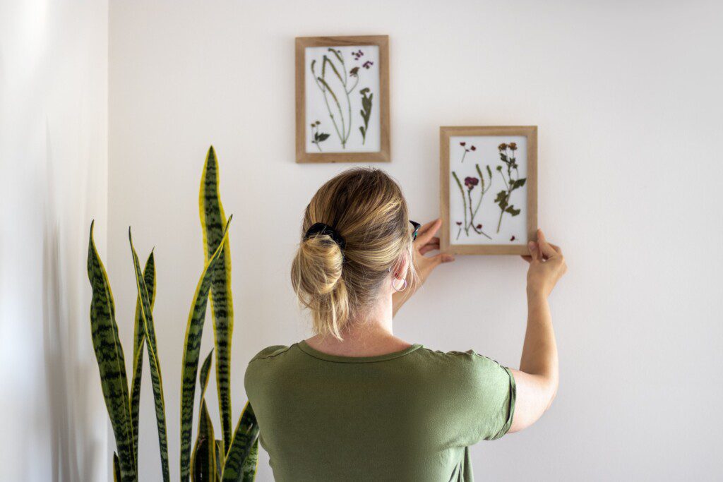 Imagem de uma mulher loira de costas pendurando um quadro na parede. 