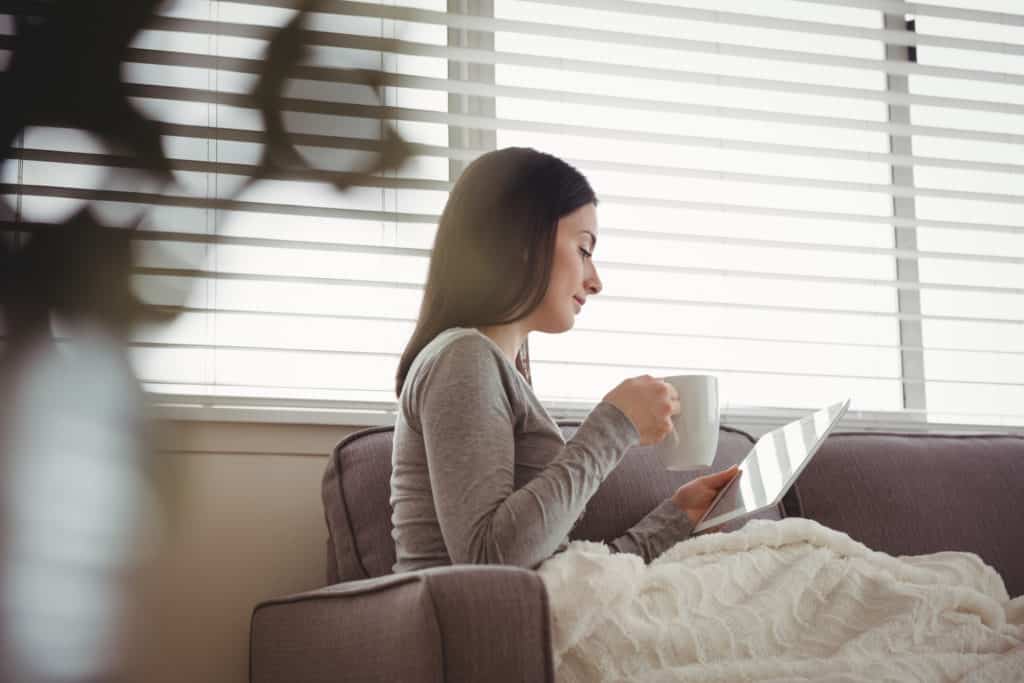 Reparo - Mulher lê em sofá próximo a janela com persiana