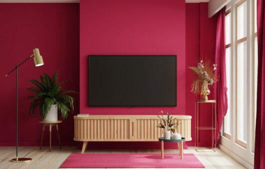 Imagem de uma sala de estar com TV, pintura de parede magenta e combinação de móveis em madeira como rack, ,mesa lateral e outros.