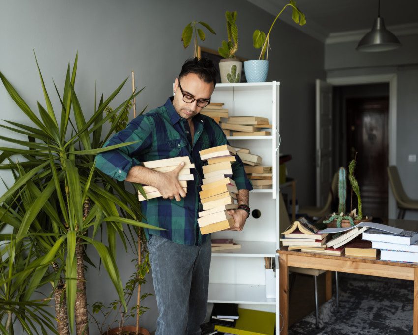 Imagem de um homem segurando vários livros nas mãos para organizá-los em uma estante.