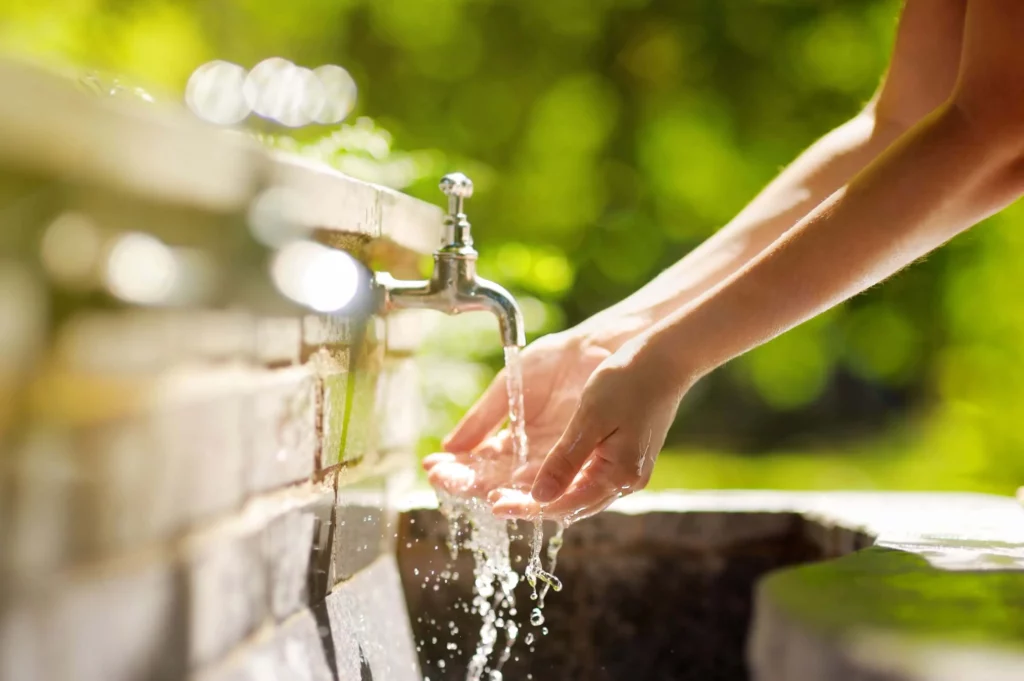 Imagem de uma pia ao ar livre com torneira ligada enquanto uma pessoa lava as mãos para ilustrar matéria sobre como fazer a troca de titularidade da Sabesp