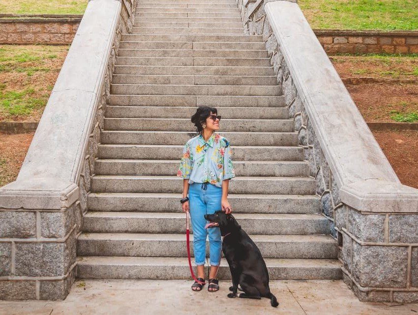 ligia souto ao lado de cachorro de pelagem preta em frente a escadaria localizada no bairro do bixiga