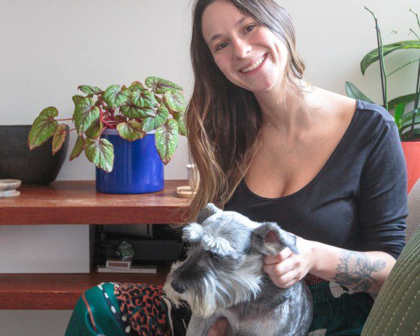 Em seu apartamento de 1 dormitório na Pompéia, a publicitária Giulia posa olhando para a câmera, sentada em um sofá, enquanto acaricia sua cachorrinha Lucy.