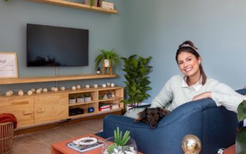 Foto que ilustra matéria sobre um apartamento no Jardim Prudência mostra a moradora do imóvel, Raissa Bóbbo, sentada em um sofá azul, com sua cachorrinha.
