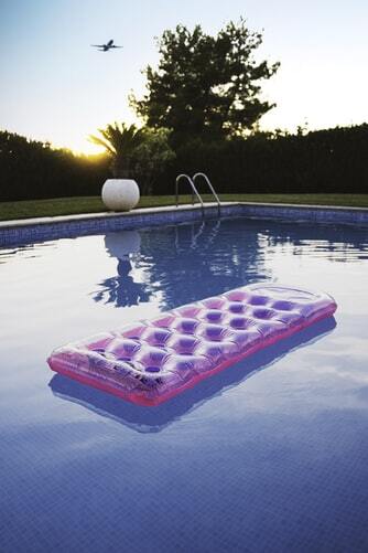 imagem de uma piscina ao pôr do sol, com uma cama inflável e cor-de-rosa flutuando na água