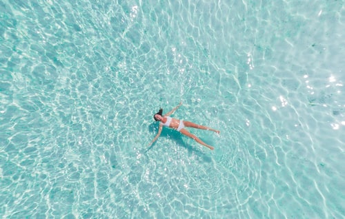 mulher de biquíni branco boiando e relaxando em uma ampla piscina azul