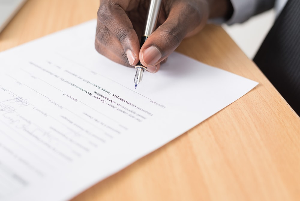 uma mão segurando uma caneta e assinando um documento, simulando uma contratação