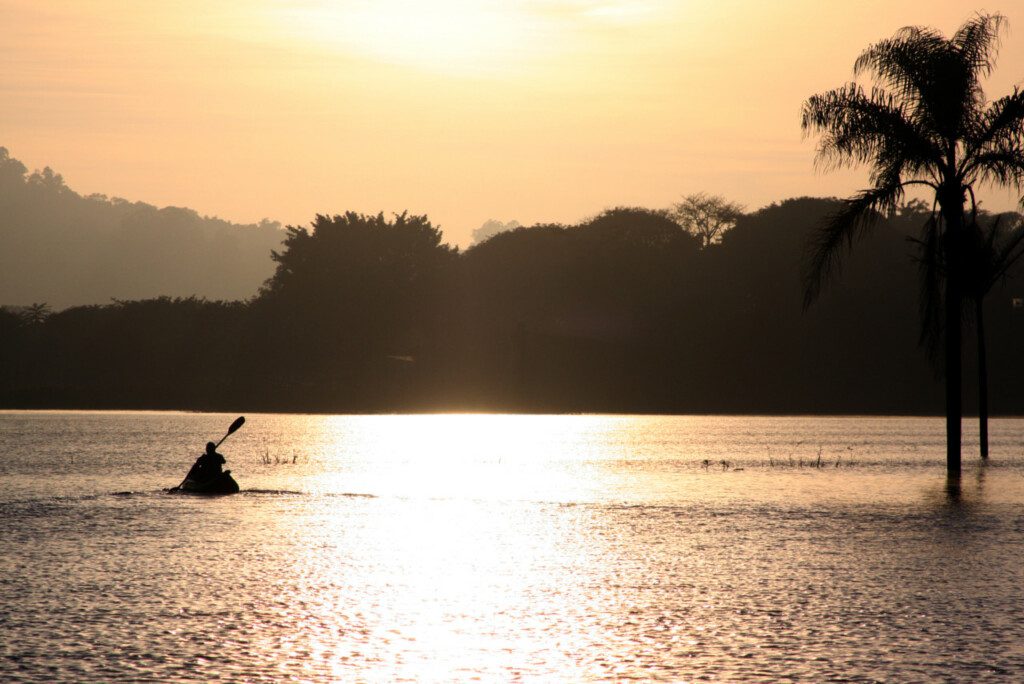 Imagem panorâmica com vista para uma pessoa andando de caiaque em um dos lagos do Parque da Cidade Jundiaí durante o pôr do sol