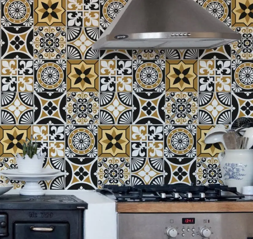 A foto mostra uma cozinha com revestimento de adesivo de azulejos. Há na imagem um fogão com coifa em cima, um porta colheres e um arranjo com planta.
