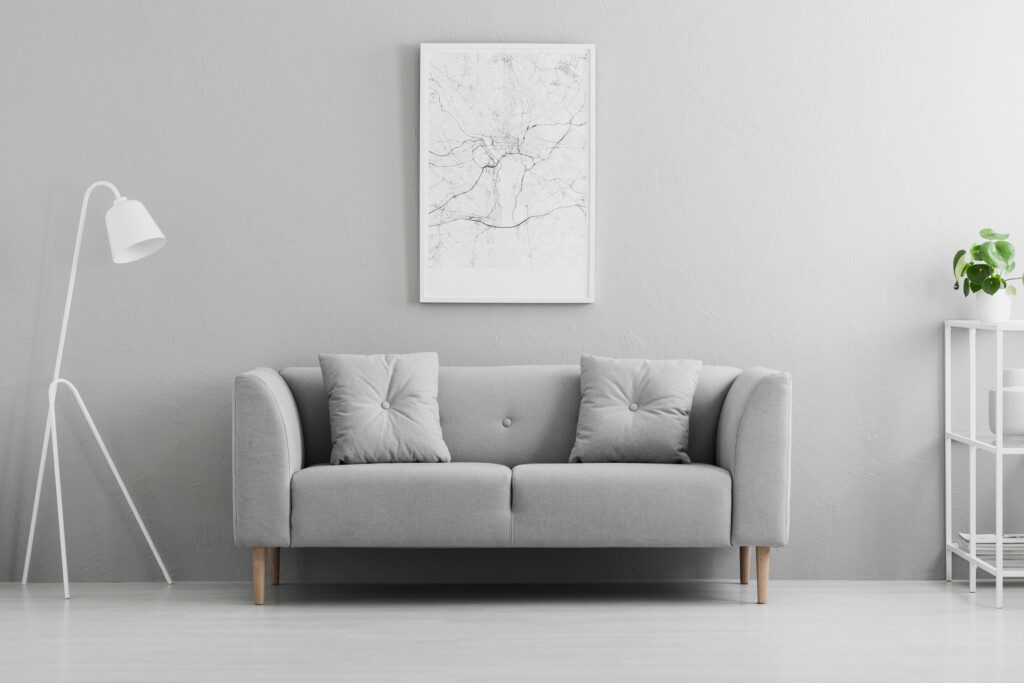 Lâmpada branca ao lado do sofá cinza no interior mínimo da sala de estar com pôster e planta. 