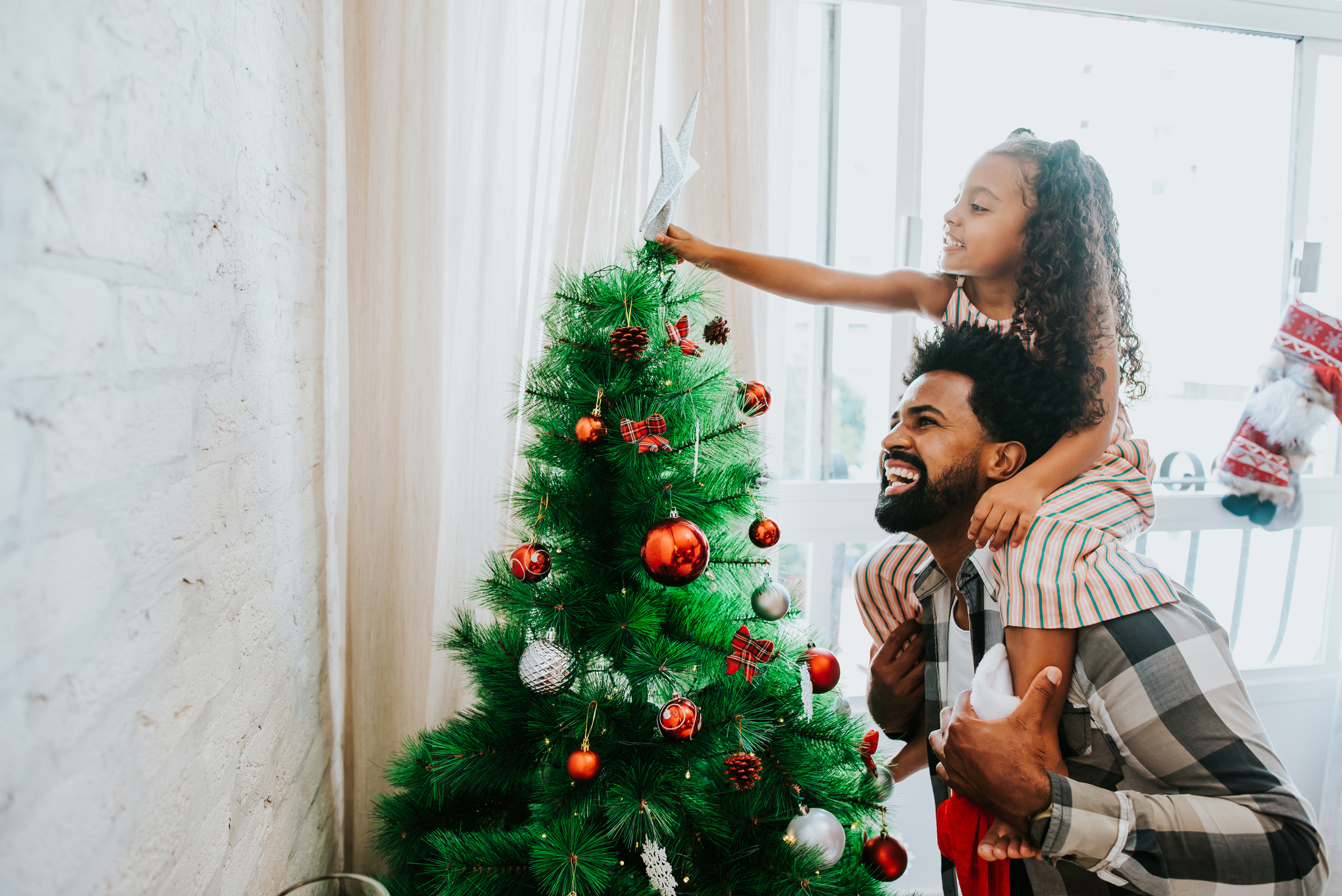 Imagem de pai e filha decorando a árvore de Natal.