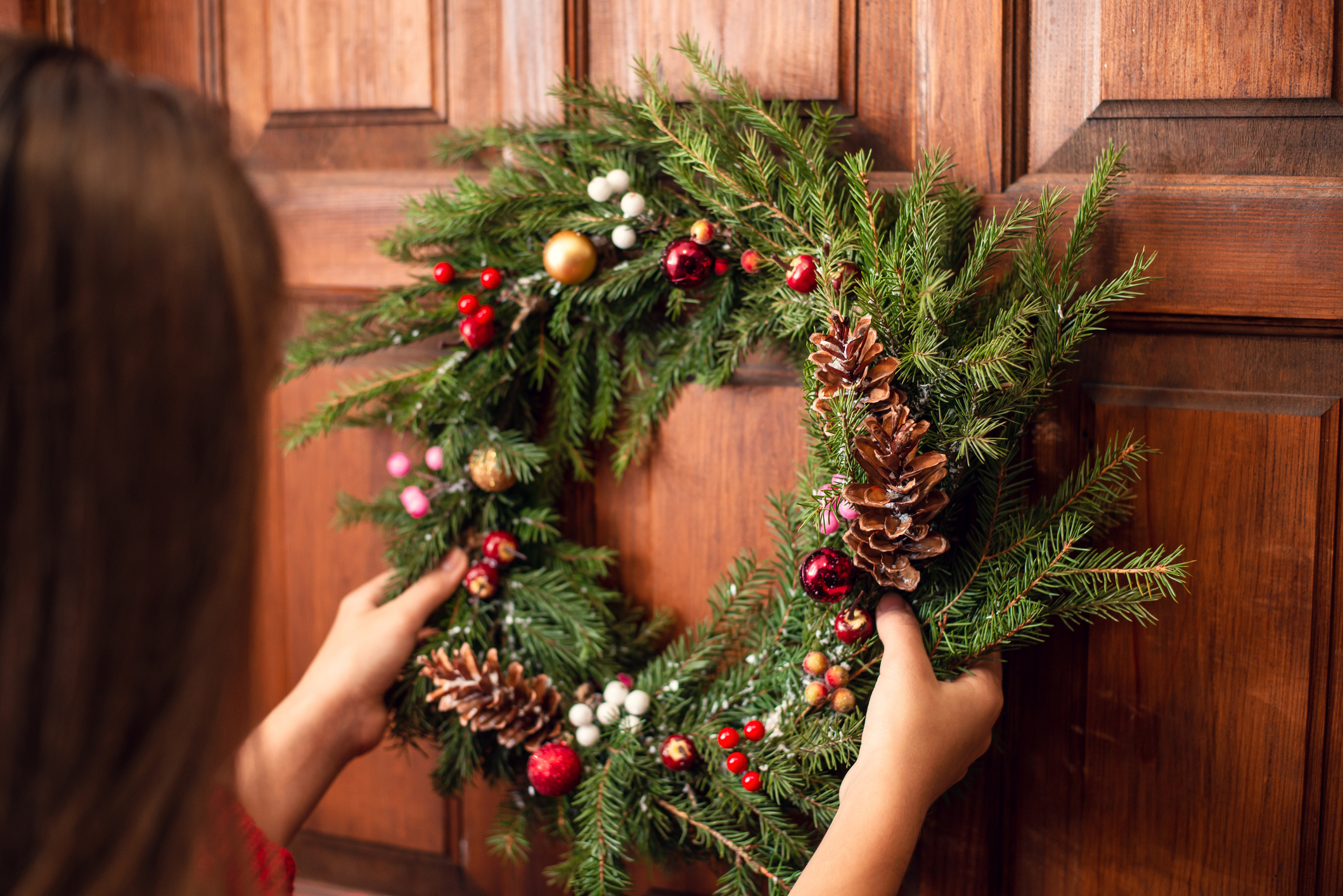 Imagem de uma jovem pendurando uma guirlanda de Natal na porta de casa.
