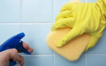 mão segurando uma esponja contra o rejunte do azulejo, enquanto outra mão segura um spray
