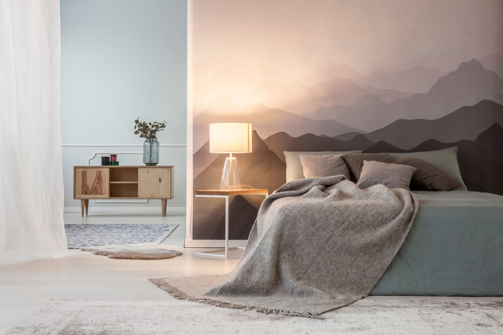 Foto que ilustra matéria sobre como colocar papel de parede mostra um quarto com a parede da cabeceira da cama coberta por uma imagem de uma cadeia de montanhas