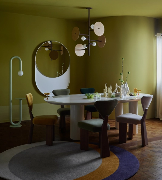 imagem mostra casa, com mesas, cadeiras, lustre pendente e espelho. Ao fundo, parede pintada na cor verde
