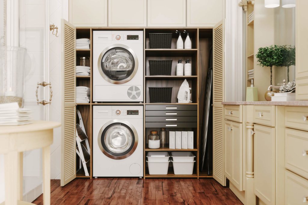 Foto que ilustra matéria sobre lavanderia pequena planejada mostra uma estrutura montada dentro de um armário embutido, com máquinas de lavar e secar, uma em cima da outra, e gavetas e prateleiras