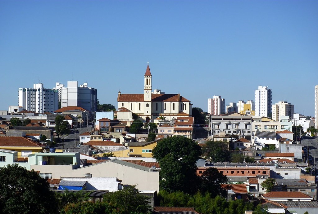 Foto que ilustra matéria sobre a Zona Leste de SP mostra uma panorâmica do bairro de Vila Matilde, com uma igreja ao fundo, no centro da tela, e um céu azul.