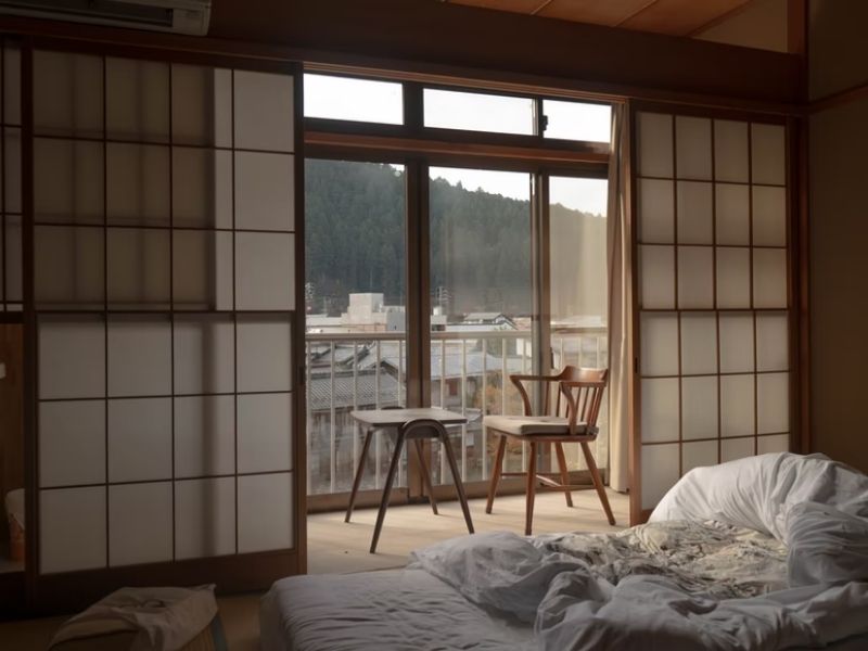 cama e cadeiras viradas para uma janela de um quarto japonês