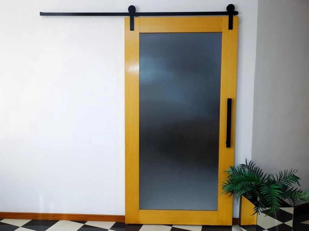 Foto de porta de correr com contorno em madeira, no centro é em vidro e os trilhos em metal preto. 