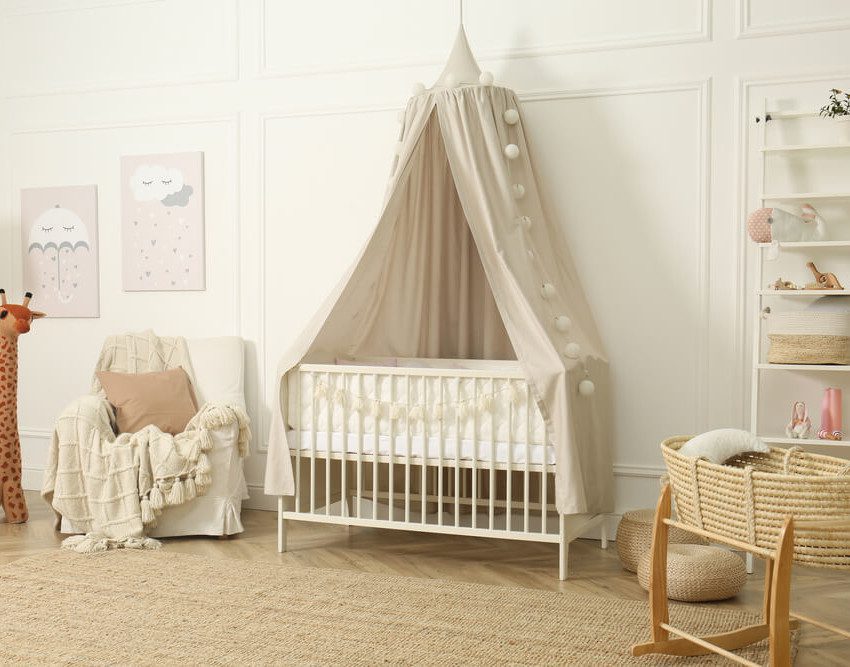 Foto que ilustra matéria sobre quarto de bebê unissex mostra um quarto com um berço branco no centro, uma poltrona de amamentação à esquerda do berço e algumas prateleiras com enfeites do lado direito.
