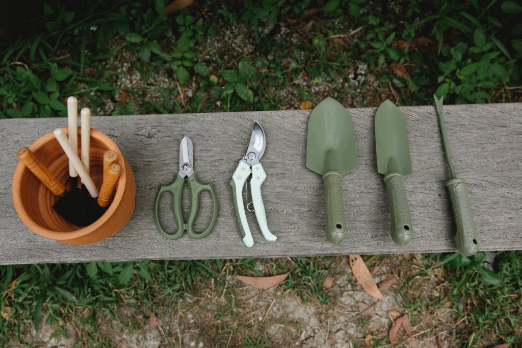 A foto ilustra os objetos básicos para fazer uma horta em casa como pá, tesoura, alicate e um vaso.