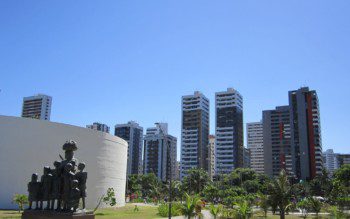 Foto que ilustra matéria sobre parques em Recife mostra uma panorâmica do Parque Dona Lindu, com uma escultura em primeiro plano, mais à esquerda, árvores à direita e grandes prédios residenciais ao fundo.