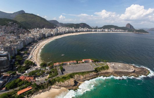 Foto que ilustra matéria sobre as praias do Rio de Janeiro mostra uma visão aérea de toda a orla da praia de Copacabana, a começar pelo Forte de Copacabana, em primeiro plano, mais abaixo na tela, seguido de toda a faixa de areia e boa parte do mar, com os prédios à esquerda e montanhas ao fundo. Entre elas os morros do Corcovado e do Pão de Açúcar