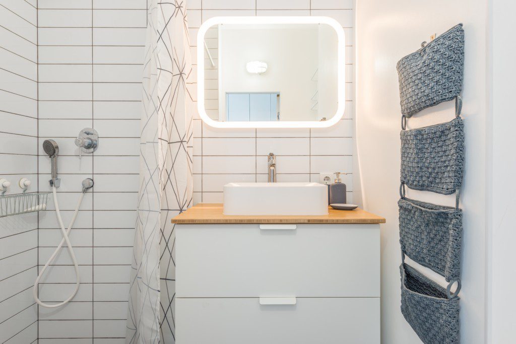 Foto de um banheiro pequeno decorado com cores neutras. Nele há: espelho retangular, pia, duas gavetas embutidas na bancada, área para banho com ducha.
