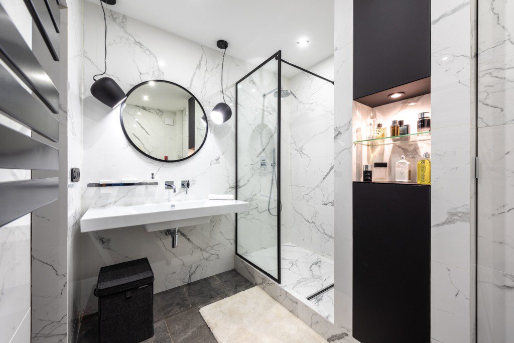 Foto de um banheiro pequeno minimalista nas cores branco e preto. Nele há uma pia com um espelho oval acima dela, um box de vidro transparente e um nicho de parede. 