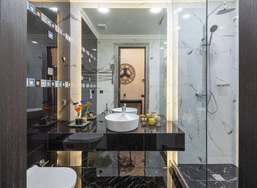 Foto de um banheiro pequeno decorado em tons de preto e branco. A bancada é preta, com uma pia branca em cima. Há também um vaso sanitário e uma área para banho.