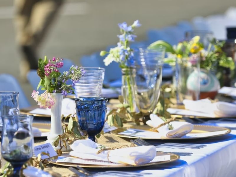 mesa posta para almoço, com toalha de mesa azul, pratos de lousa e copos de vidro