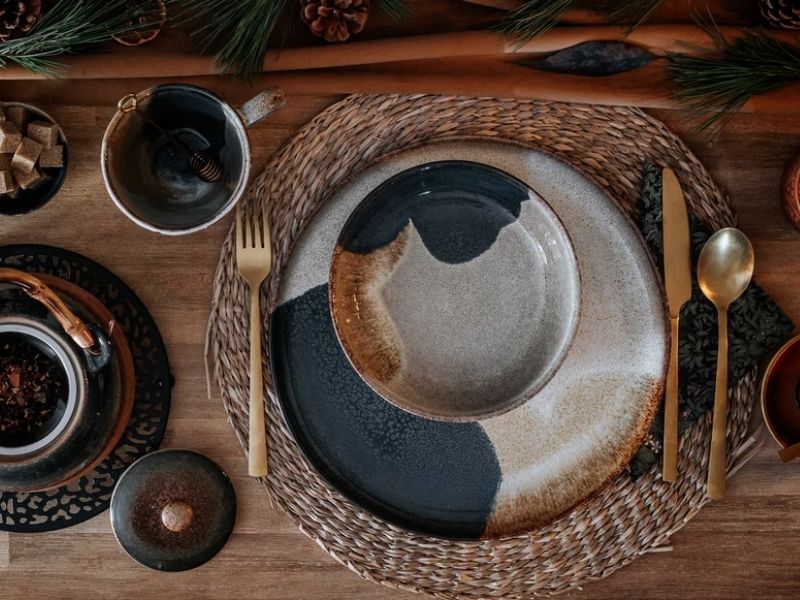 mesa posta para um café da manhã, em uma mesa de madeira, com jogo americano redondo marrom, prato manchado, bowl de comida manchado e talheres.