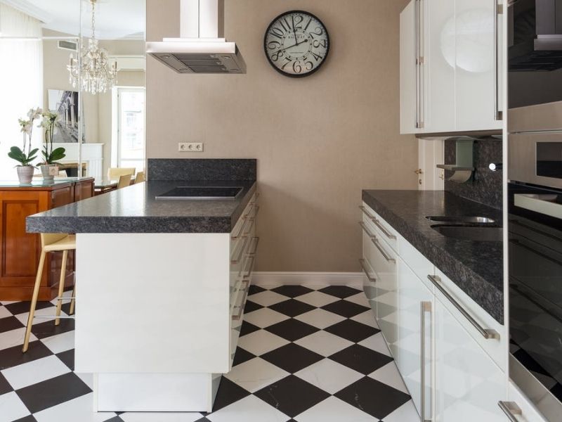 cozinha com balcão dividindo ambientes, piso preto e branco em estilo xadrez, um relógio na parede ao fundo