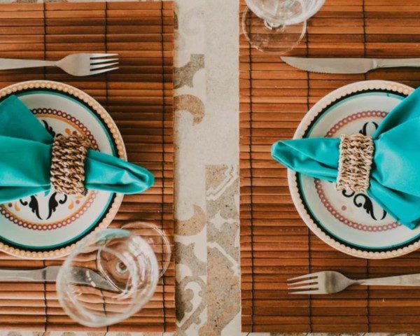 pratos e talheres sobre um jogo americano em uma mesa. Um guardanapo azul está acima do prato.