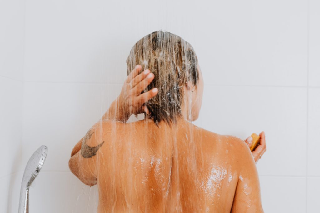Foto de uma mulher de costas tomando banho para ilustrar uma das dicas para amenizar a crise hídrica e energética que estamos vivendo que é tomar banhos mais curtos