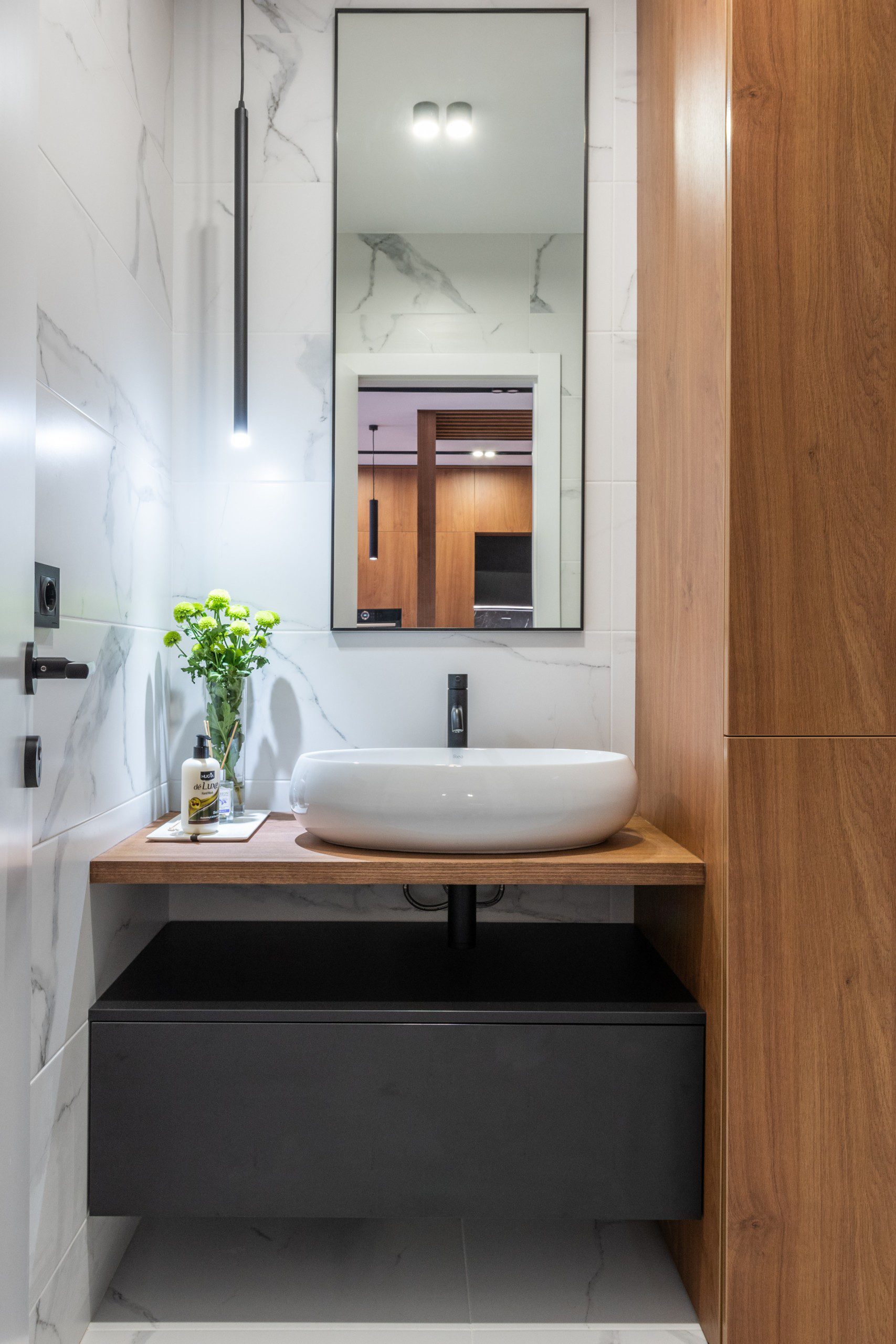 A foto mostra um banheiro pequeno decorado com espelho grande em formato retangular com moldura preta.