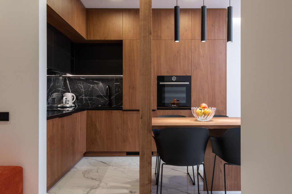 Armário de cozinha em formato de L em cor de madeira com detalhes em preto sem puxadores. 