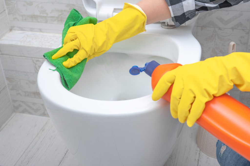 pessoa aplicando detergente no vaso sanitário com luvas