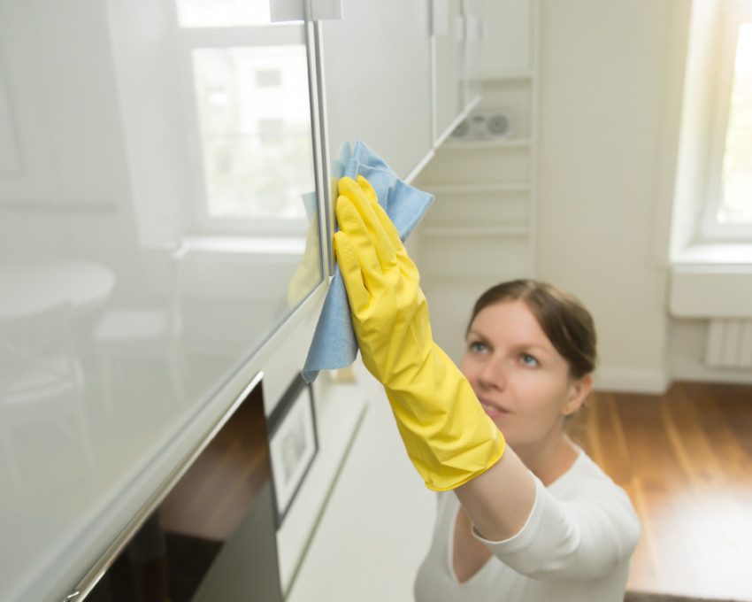 Mulher com uma camiseta branca limpando o armário da cozinha com produtos caseiros que acabam com formigas.