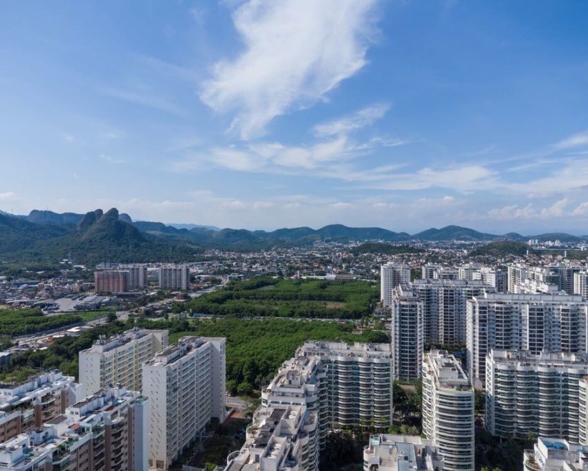 Foto que ilustra matéria sobre a Zona Oeste do RJ mostra uma vista aérea de Jacarepaguá, com grandes condomínios de prédios residenciais em primeiro plano e montanhas ao fundo.