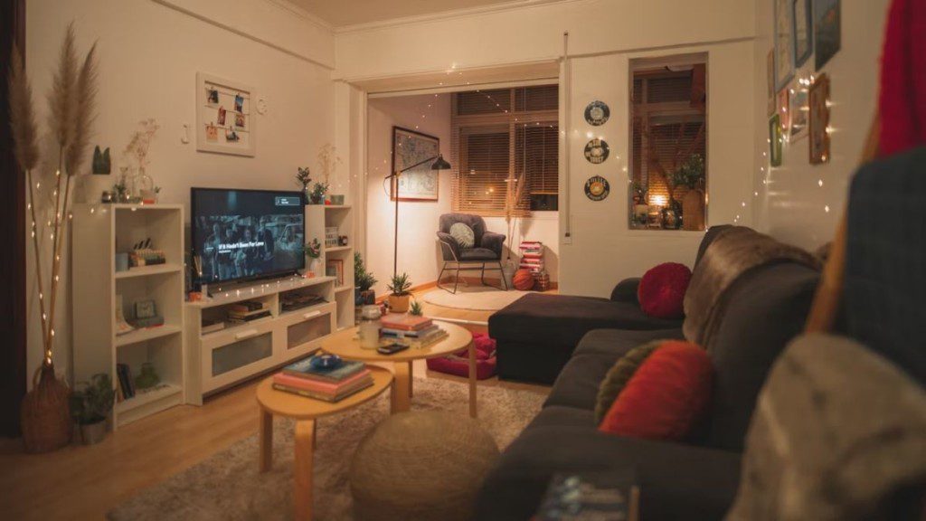 Sala de televisão aconchegante, com sofá em L, luzes de natal nas paredes, um móvel grande e televisão de plasma.