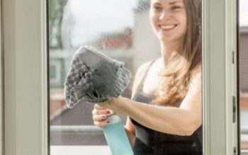 mulher sorrindo enquanto faz atividades de faxina, como limpar vidro de janela pelo lado de fora