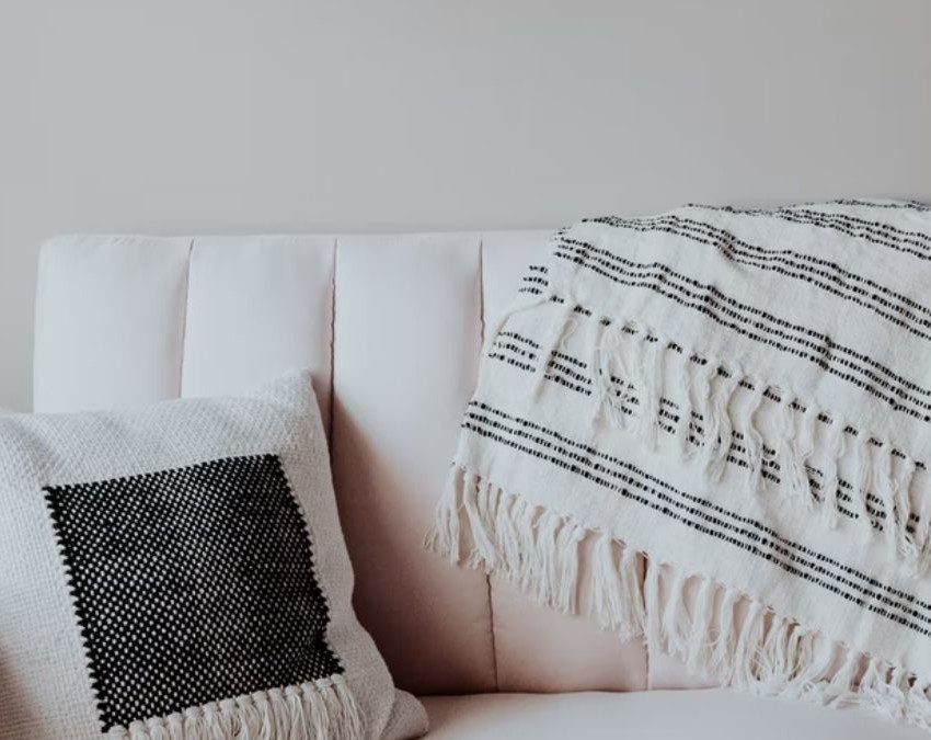 sofá branco com almofada e manta no encosto, capa do conteúdo sobre como usar manta no sofá