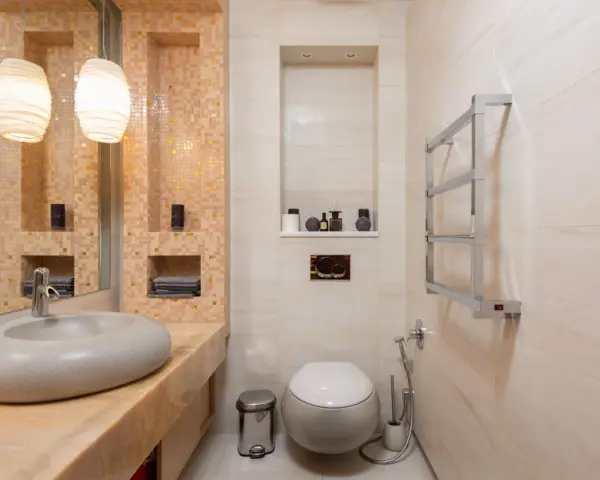 Imagem de um lavabo moderno com uma vaso sanitário super estiloso, parede com porcelanatos em tons de creme, uma pia moderna em formato circular com uma pedra cinza e uma luminária.