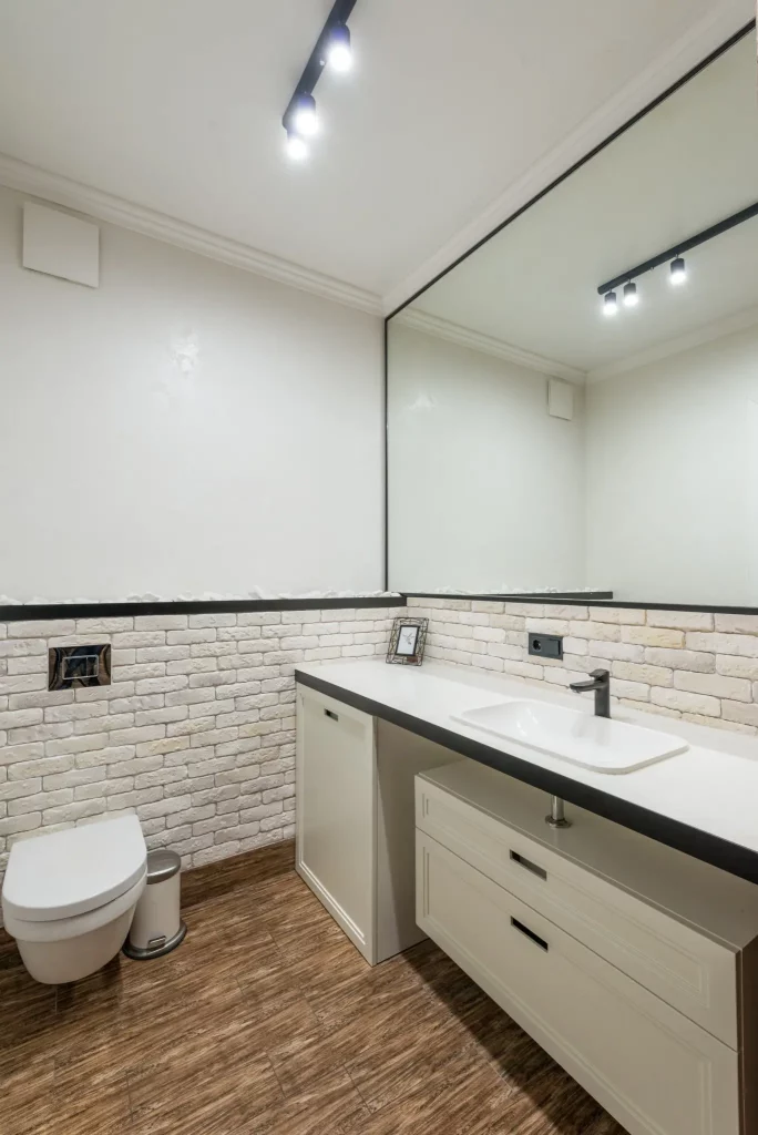 A imagem mostra um lavabo moderno minimalista. Nele há um vaso sanitário, uma pia com armários e gavetas embaixo, além de um espelho retangular ocupando uma das paredes.