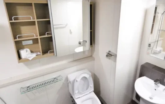 A imagem mostra um lavabo pequeno com decoração moderna em tons neutros e iluminação com pendente. Na imagem há uma privada, um apoio lateral, uma pia e uma estante com porta de espelho.