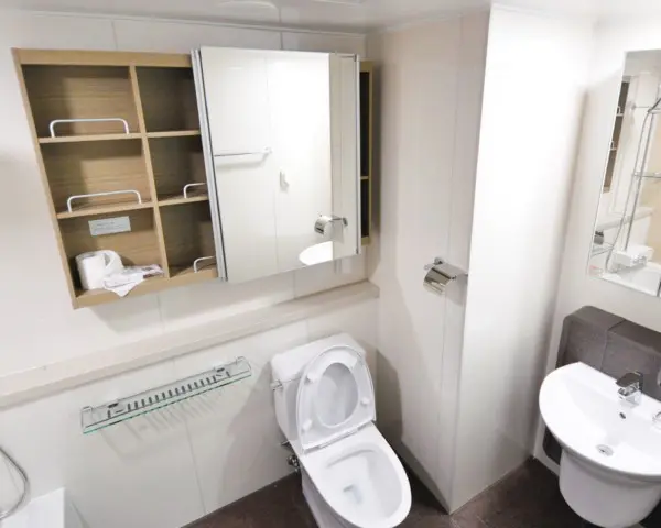 A imagem mostra um lavabo pequeno com decoração moderna em tons neutros e iluminação com pendente. Na imagem há uma privada, um apoio lateral, uma pia e uma estante com porta de espelho.