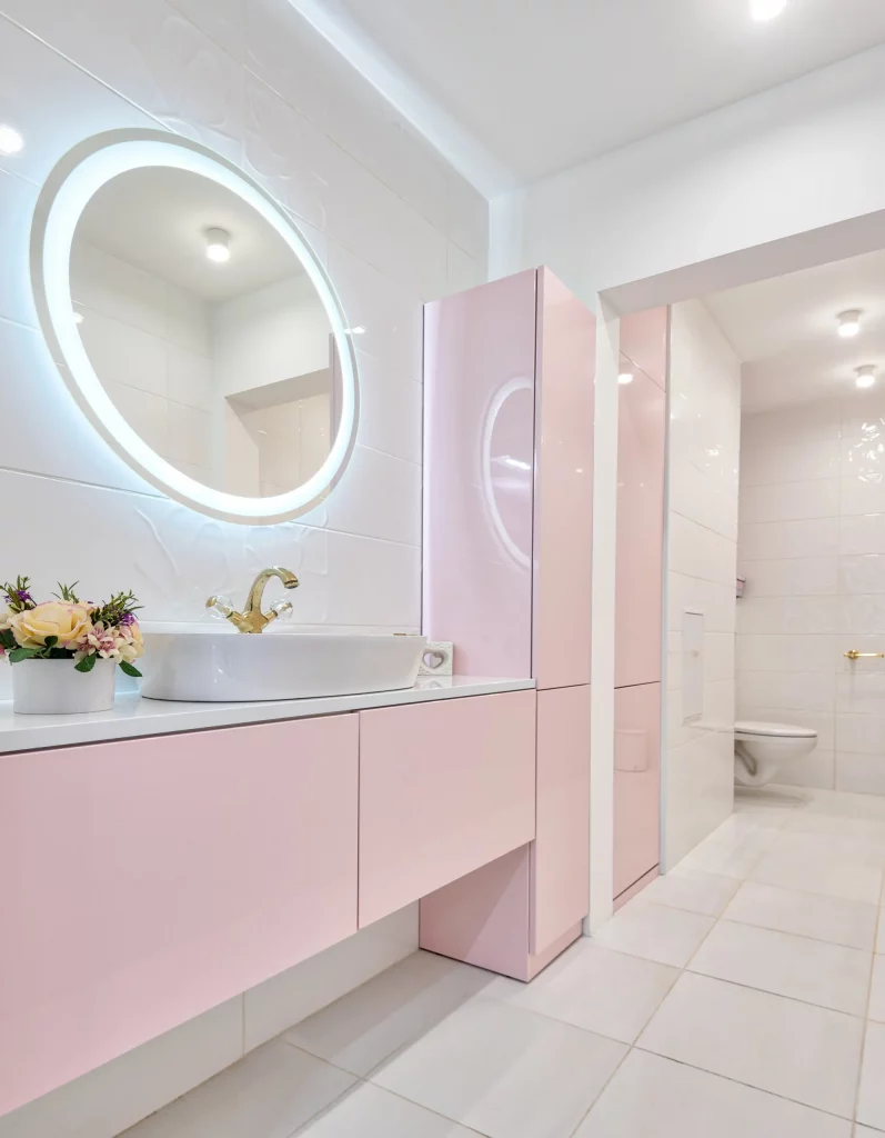 A imagem mostra um lavabo com móveis planejados. Nele há uma pia com armário embutido embaixo, espelho redondo com luz ao redor e um armário grande ao lado da pia.